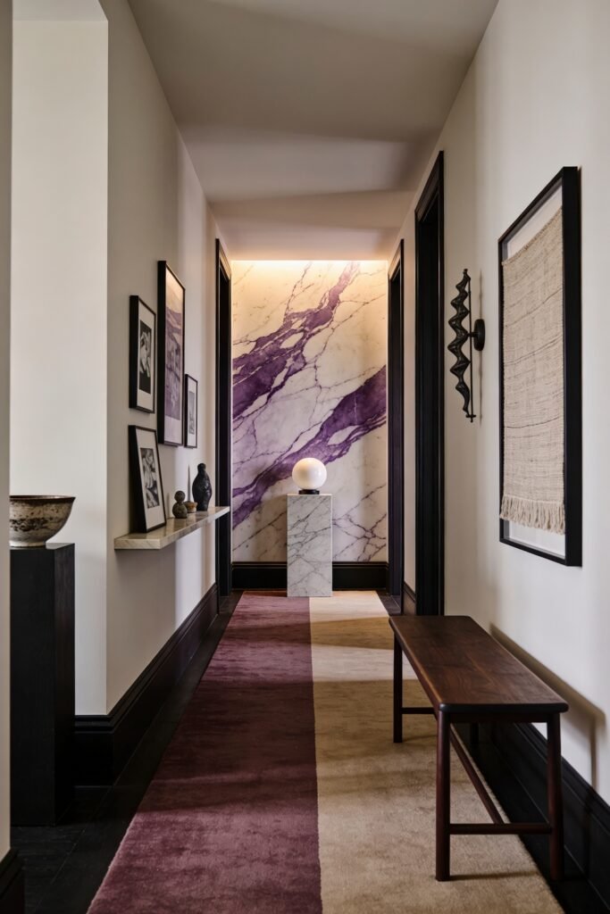 Narrow corridor with a long runner dark trim and a backlit marble wall with soft purple veining