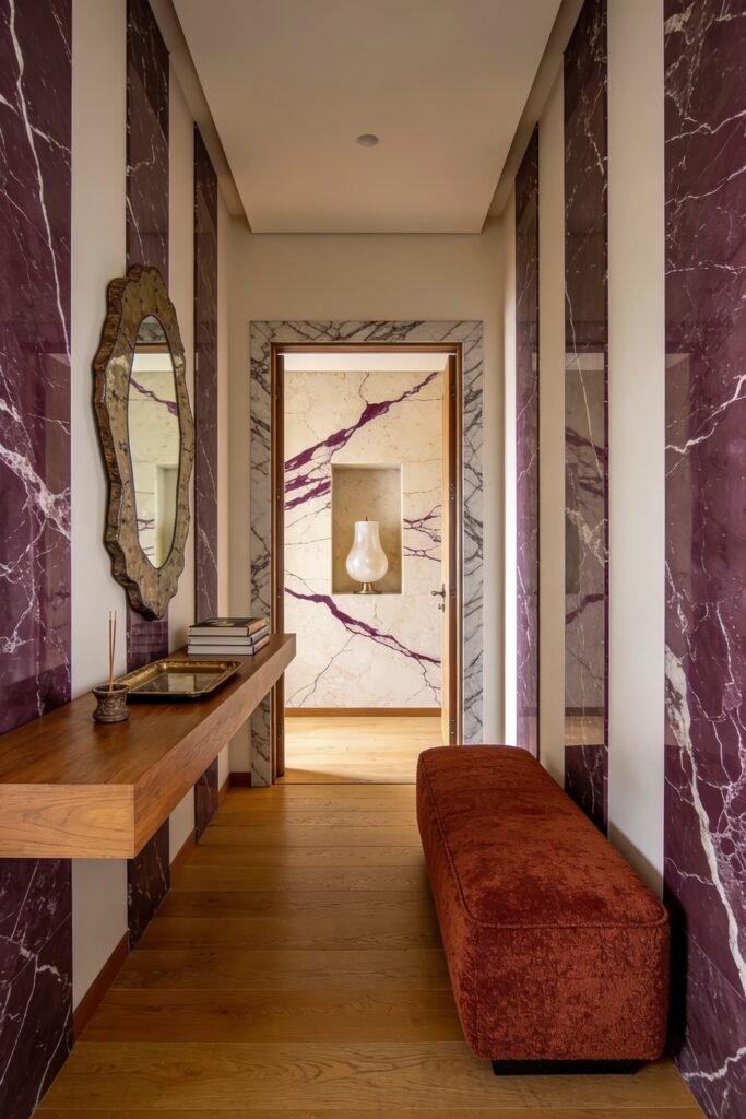 Narrow hallway with rich purple marble wall panels a floating wood console and a rust upholstered bench on oak floors