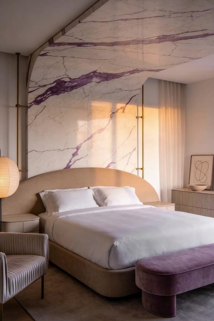 Serene bedroom with a curved upholstered bed and bench set against a large marble wall and ceiling with lavender veining