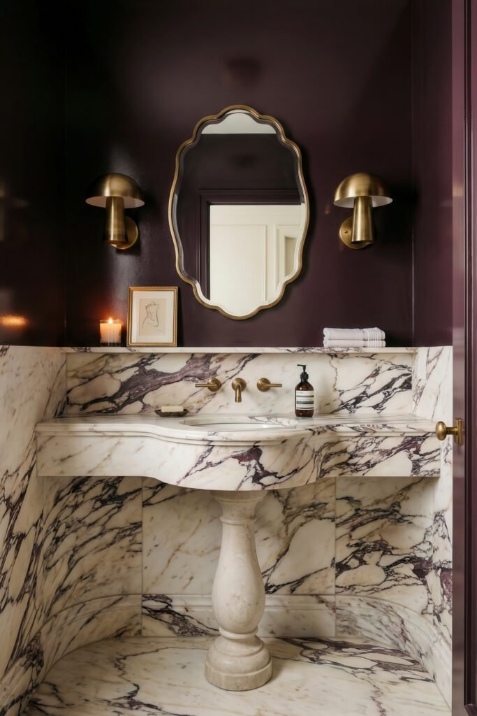 Dramatic powder room with a sculpted marble sink brass sconces and a scalloped mirror against deep plum walls