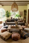 Living room with Afro Cultural Patterns, oversized woven pendant, wood beams, mudcloth pillows, leather poufs, jute rug, plants, and arched windows.