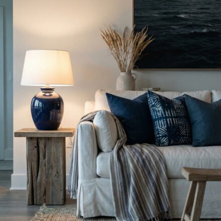 Coastal Summer Aesthetic Ideas for a Breezy Apartment White slipcovered sofa with navy pillows, striped throw, blue ceramic lamp, ocean art, and jute rug creating a refined coastal summer aesthetic in a serene living room.