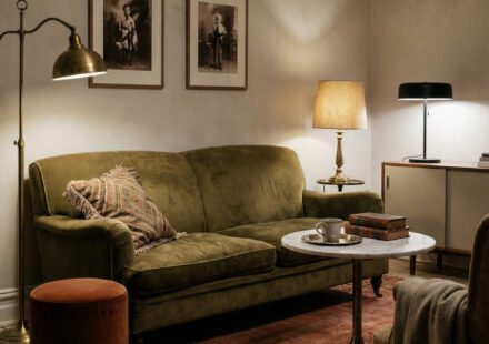 Moody green and rust living room with an olive velvet sofa, brass floor lamp, rust ottoman, vintage rug, marble coffee table, and warm layered lighting.