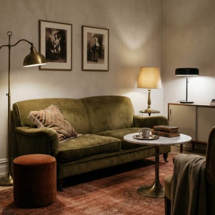 Moody green and rust living room with an olive velvet sofa, brass floor lamp, rust ottoman, vintage rug, marble coffee table, and warm layered lighting.