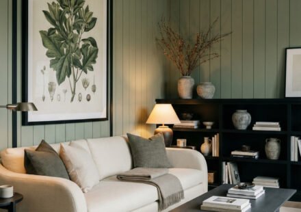 Moody living room with sage green paneled walls, black trim, cream sofa, black coffee table, styled shelving, and botanical art for Sage Green And Black Living Room Ideas.