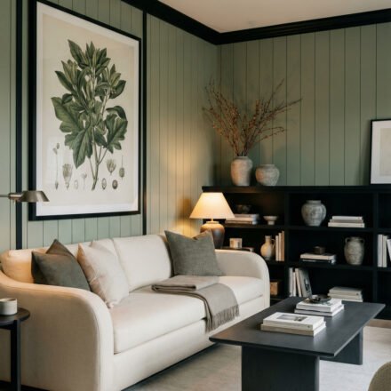 Sage Green And Black Living Room Ideas for a Layered Look Moody living room with sage green paneled walls, black trim, cream sofa, black coffee table, styled shelving, and botanical art for Sage Green And Black Living Room Ideas.