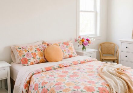 Warm bedroom with coral and peach floral duvet, matching pillows, white nightstands, a cane chair, and soft spring bedding for a bright, cheerful seasonal refresh.