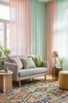Pastel pink and mint sheer curtains, gray loveseat, floral pillows, and a colorful rug create playful spring living room décor with a light, collected feel.
