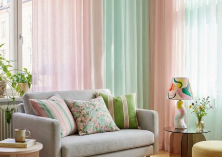 Pastel pink and mint sheer curtains, gray loveseat, floral pillows, and a colorful rug create playful spring living room décor with a light, collected feel.