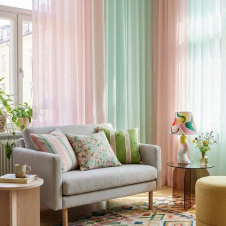 Pastel pink and mint sheer curtains, gray loveseat, floral pillows, and a colorful rug create playful spring living room décor with a light, collected feel.