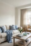 Summer Living Room Decor for a Light and Lively Space Airy living room with a cream sofa, soft blue pillows, sheer curtains, wicker chair, and light wood coffee table for elegant Summer Living Room Decor.