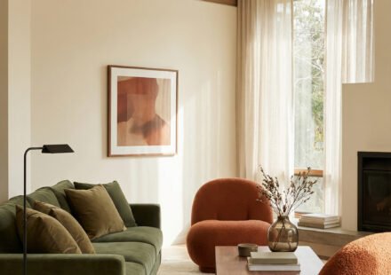 Olive green sofa with burnt orange boucle chairs, wood coffee table, beige rug, tall sheer curtains and fireplace in a warm Green Burnt Orange Living Room