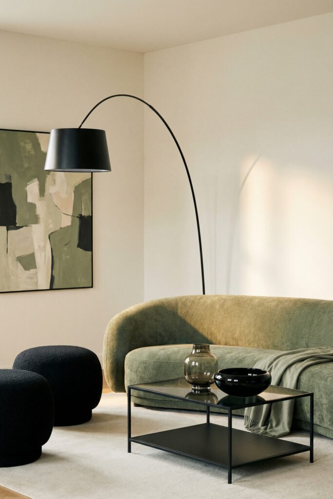 Sage Green And Black Living Room Ideas for a Layered Look 24 Close-up of a curved sage sofa with black arc lamp, black boucle poufs, glass coffee table, and soft abstract wall art.