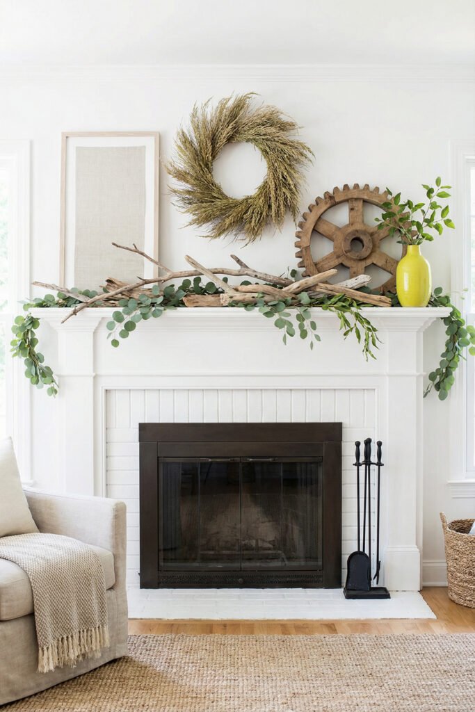 White fireplace with driftwood, eucalyptus garland, a wheat wreath, wood wheel, and yellow vase for organic rustic summer mantle décor.
