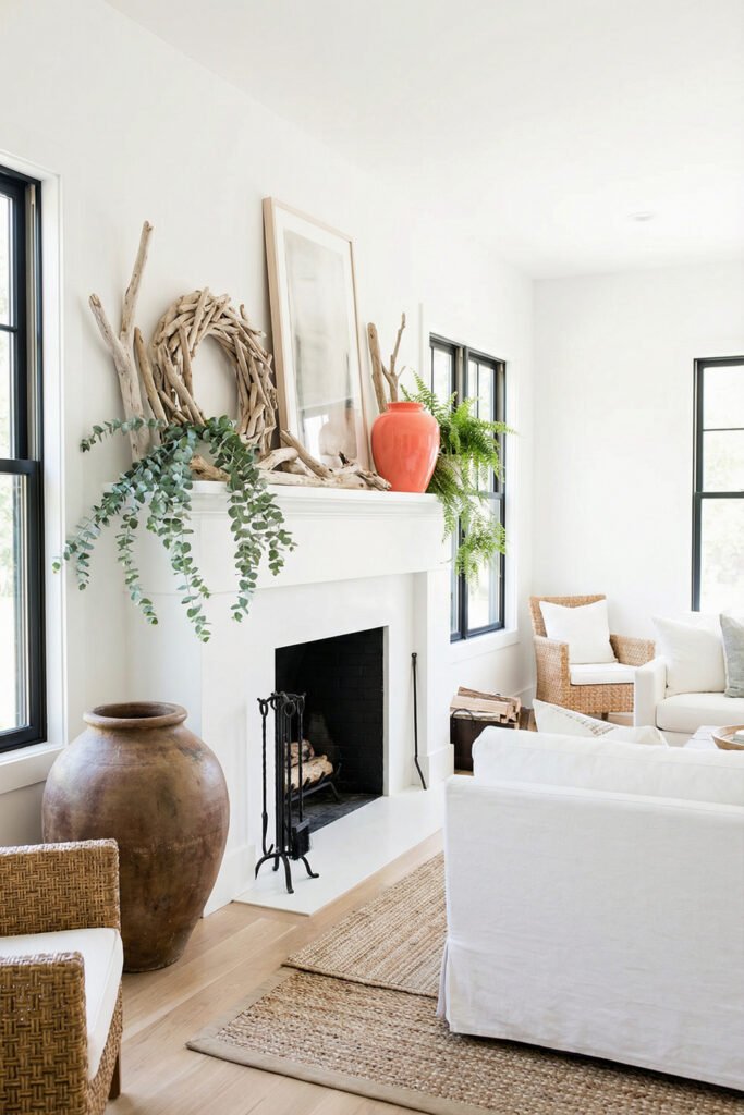 Bright white fireplace styled with driftwood, a sculptural wreath, coral vase, eucalyptus, and a fern for airy natural summer mantle décor.
