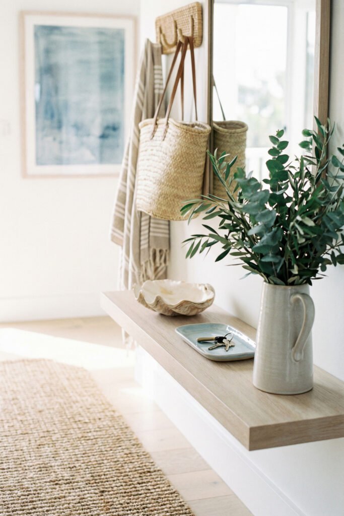Summer Décor Ideas for an Airy, Collected Home 23 Minimal entry hall with floating wood shelf, woven rug, keys tray, greenery in ceramic pitcher, and straw tote for summer decor.