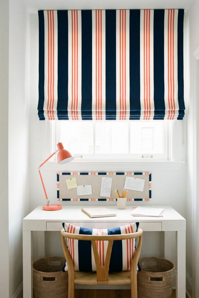 Narrow white desk under a striped roman shade with coral lamp, pinboard, and woven baskets in a polished Summer Office Decor nook.
