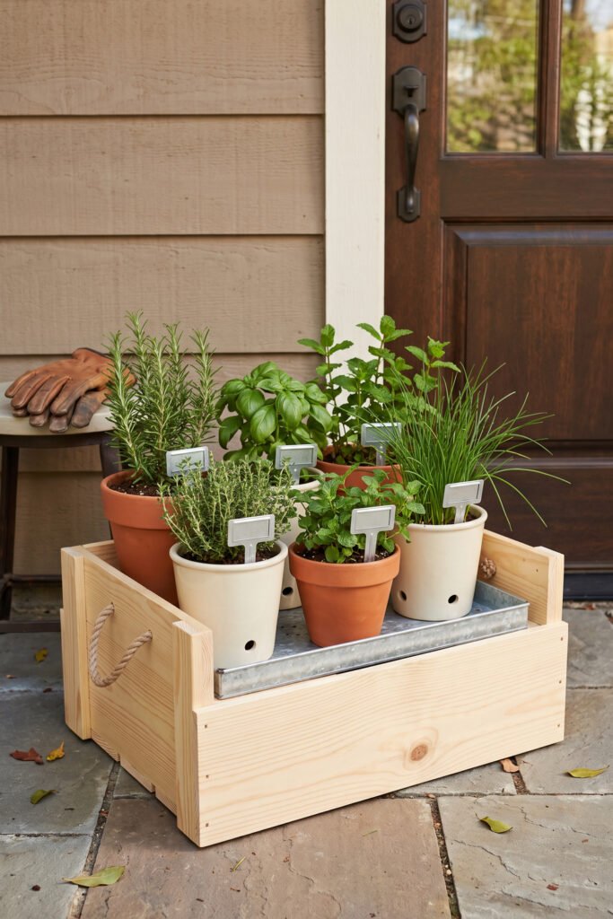 Natural wood crate with rope handles holding individually potted herbs on a galvanized tray beside an exterior door.